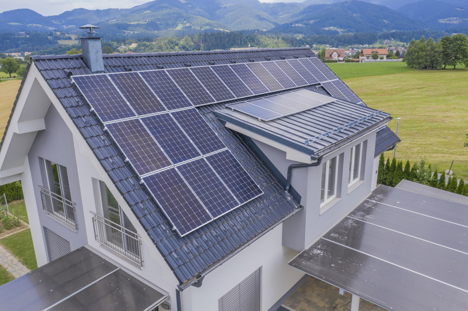 Maison moderne avec plusieurs panneaux solaires installés sur le toit, dans un paysage rural montagneux.